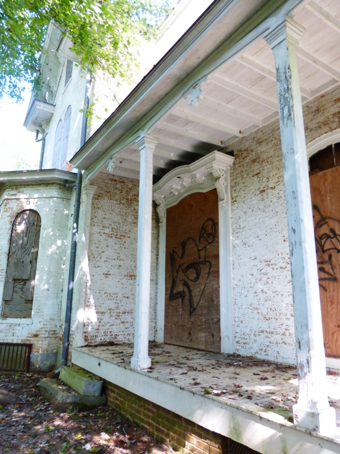 View of the front porch and the original front door.  Note the detailed woodwork around the door and the graffiti at close proximity to the original workmanship.